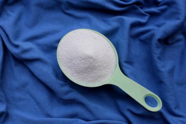 Detergent powder in measuring spoon on cloth before washing. Laundry concept.