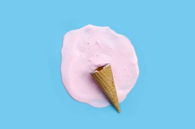 Mavi zemin üzerinde waffle külahı olan dondurma topu eritiliyor.