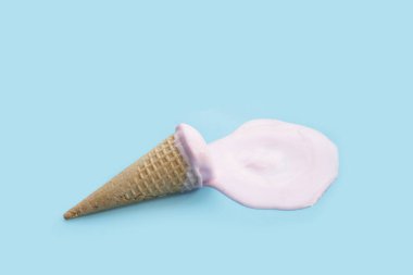 Mavi zemin üzerinde waffle külahı olan dondurma topu eritiliyor.