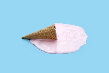 Mavi zemin üzerinde waffle külahı olan dondurma topu eritiliyor.
