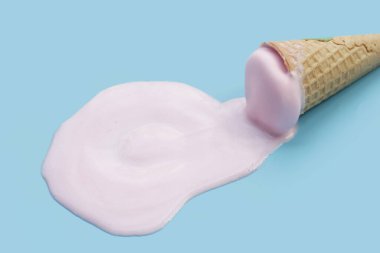 Mavi zemin üzerinde waffle külahı olan dondurma topu eritiliyor.