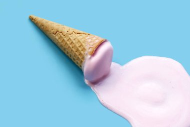 Mavi zemin üzerinde waffle külahı olan dondurma topu eritiliyor.