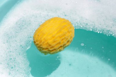 Sarı banyo süngeri sabun köpüğüyle mavi suda yüzüyor.