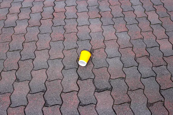 stock image Yellow coffee paper cup with a black lid on the street pavement floor