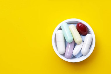 Sarı arka planda renkli kapsüller ve haplar.