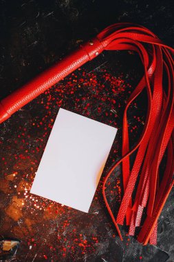 Kart maketi, beyaz kağıt bdsm oyuncaklarının maketi, kırmızı parıltılı siyah arka planda kırmızı deri kırbaç.