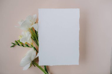 white paper mockup with texture on festive peach background with flowers white and yellow colors,wedding invitation mockup, top view, spring mockup