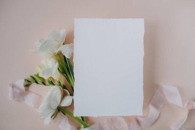 white paper mockup with texture on festive peach background with flowers white and yellow colors,wedding invitation mockup, top view, spring mockup