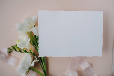 white paper mockup with texture on festive peach background with flowers white and yellow colors,wedding invitation mockup, top view, spring mockup
