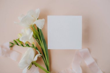 white paper mockup with texture on festive peach background with flowers white and yellow colors,wedding invitation mockup, top view, spring mockup
