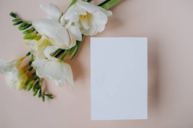 white paper mockup with texture on festive peach background with flowers white and yellow colors,wedding invitation mockup, top view, spring mockup