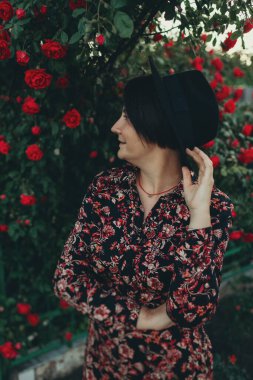 Siyah şapkalı ve elbiseli bir kadın gül çalılıklarında duruyor. 40 'larında bir kadın portresi.
