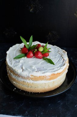 Siyah arka planda kremalı ve çilekli bisküvi keki.