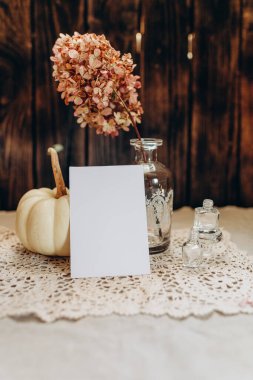 Beyaz bir balkabağı ve kurumuş çiçeklerin arka planında klasik tarzda davetiyeler.