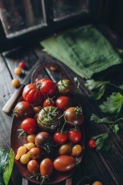 Durgun hayat, farklı domates çeşitleri ahşap bir masaya saçılmış, yumuşak sabah ışığı, üst görünüm