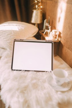 Battaniye ve yastık arka planında beyaz ekranı olan bir tabletin kopyası