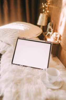 Battaniye ve yastık arka planında beyaz ekranı olan bir tabletin kopyası