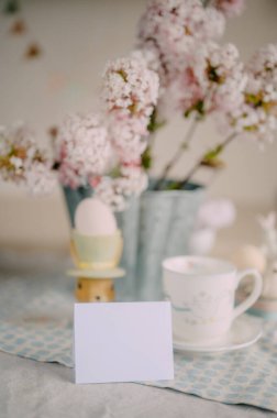 Zarif Paskalya Masası üzerinde Pembe Leylak Çiçekleri ve Festivalsel Dekorasyonlarla mokcup kartı