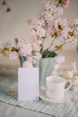 Zarif Paskalya Masası üzerinde Pembe Leylak Çiçekleri ve Festivalsel Dekorasyonlarla mokcup kartı