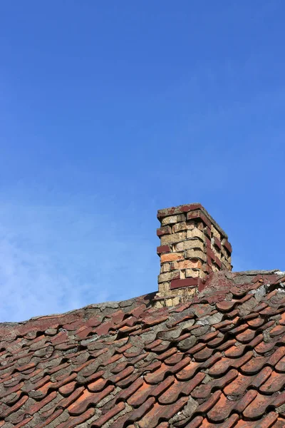 Roof top with old tiles and a stone chimney against a blue sky