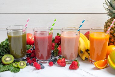 Güzel, sağlıklı yeşil, karışık çilek, çilekli muz, ve cam kavanozda mango meyveli smoothie, kağıt samanla kaplı taze malzemeler.