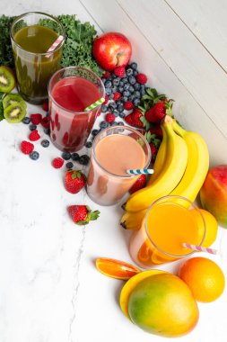 Güzel, sağlıklı yeşil, karışık çilek, çilekli muz, ve cam kavanozda mango meyveli smoothie, kağıt samanla kaplı taze malzemeler.