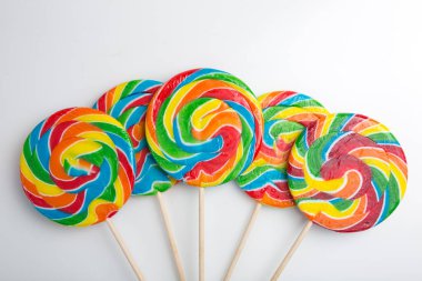 Beyaz arka planda renkli şekerleme lolipopu. Gökkuşağı tatlı deseni etrafında uçan çubuk üzerinde.