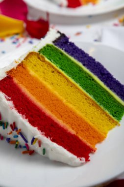 Gökkuşağı katmanlı pasta peynir kremalı krema ve beyaz arka planda çok renkli şeker serpiştirilmiş.