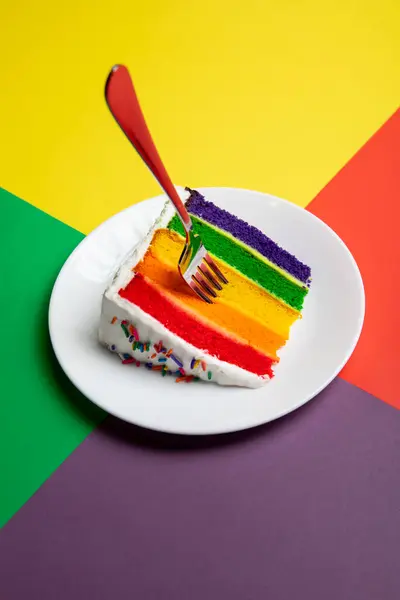 Gökkuşağı katmanlı pasta peynir kremalı krema ve beyaz arka planda çok renkli şeker serpiştirilmiş.