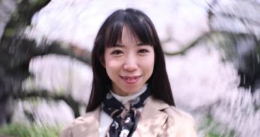 Tokyo 'da kiraz çiçeğinin arkasındaki Japon kadın portresinin 2x yavaş çekimi. Yüksek kalite 4K görüntü. Chiyoda bölgesi Tokyo 03.30.2023