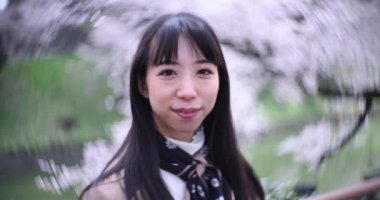 Tokyo 'da kiraz çiçeğinin arkasındaki Japon kadın portresinin 2x yavaş çekimi. Yüksek kalite 4K görüntü. Chiyoda bölgesi Tokyo 03.30.2023