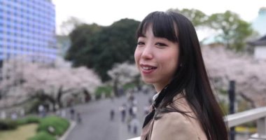 Tokyo 'da kiraz çiçeğinin arkasındaki Japon kadın portresinin 2x yavaş çekimi. Yüksek kalite 4K görüntü. Chiyoda bölgesi Tokyo 03.30.2023