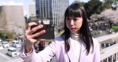 Kiraz çiçeğinin arkasındaki Japon kadının selfie portresi. Yüksek kalite 4K görüntü. Chiyoda bölgesi Tokyo 03.30.2023