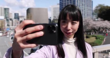 Kiraz çiçeğinin arkasındaki Japon kadının selfie portresi. Yüksek kalite 4K görüntü. Chiyoda bölgesi Tokyo 03.30.2023