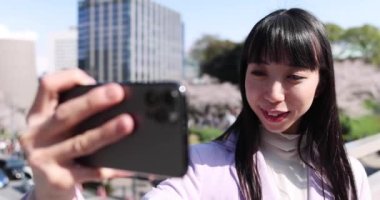 Kiraz çiçeğinin arkasındaki Japon kadının selfie portresi. Yüksek kalite 4K görüntü. Chiyoda bölgesi Tokyo 03.30.2023