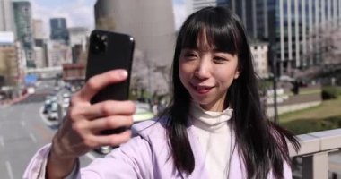 Kiraz çiçeğinin arkasındaki Japon kadının selfie portresi. Yüksek kalite 4K görüntü. Chiyoda bölgesi Tokyo 03.30.2023