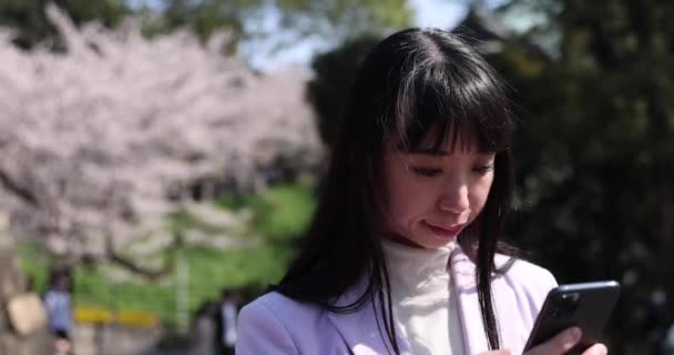Ein Porträt Einer Japanerin Die Ihr Smartphone Hinter Einem Kirschblütenhandheld — Stockvideo
