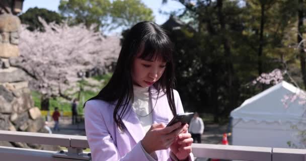 一张日本女人手持樱花后打电话给智能手机的肖像高质量的4K镜头 Chiyoda District Tokyo Japan 2023 — 图库视频影像