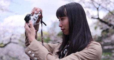 Kiraz çiçeğinin arkasında aynasız kamerayla çekim yapan Japon kadının portresi. Yüksek kalite 4K görüntü. Chiyoda bölgesi Tokyo 03.30.2023