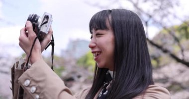 Kiraz çiçeğinin arkasında aynasız kamerayla çekim yapan Japon kadının portresi. Yüksek kalite 4K görüntü. Chiyoda bölgesi Tokyo 03.30.2023