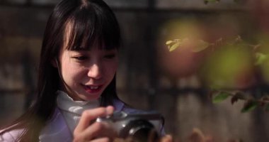 Kiraz çiçeğinin arkasında aynasız kamerayla çekim yapan Japon kadının portresi. Yüksek kalite 4K görüntü. Chiyoda bölgesi Tokyo 03.30.2023