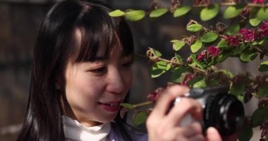 Kiraz çiçeğinin arkasında aynasız kamerayla çekim yapan Japon kadının portresi. Yüksek kalite 4K görüntü. Chiyoda bölgesi Tokyo 03.30.2023