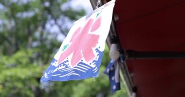 Yazın Tokyo 'da yeşil ağacın arkasında bir Japon mağazası perdesi. Yüksek kalite 4K görüntü. Chofu Bölgesi Tokyo 07.07.2023 Bir dükkan perdesi metni üzerinde çeviri.