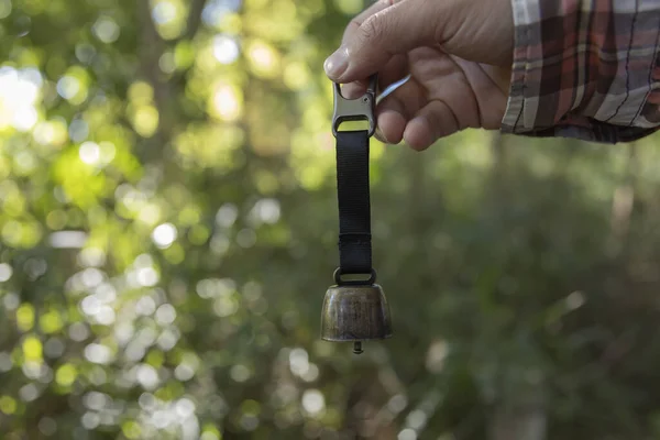 A bear bell with hand at the green forest in Autumn. High quality photo. This bell is the product to avoid a bear at the forest.