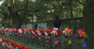 Heykel bekçisi kırmızı şapkalı ve siyah karga gündüz vakti. Tokyo Minato Bölgesi - 07.25.2019: Geleneksel tapınakta bulunan eski bir heykel.