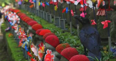 Heykel bekçisi kırmızı şapkalı ve siyah karga gündüz vakti. Tokyo Minato Bölgesi - 07.25.2019: Geleneksel tapınakta bulunan eski bir heykel.