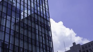 İş kasabasındaki ofis binasını yansıtan hareket eden bulutlar. Yüksek kalite 4K görüntü. Shinjuku Bölgesi Nishishinjuku Tokyo Japonya 06.27.2025 Tokyo 'nun merkezidir.. 