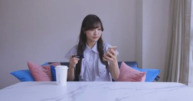 Oturma odasında elinde Card ve Smartphone olan bir Japon kadın. Yüksek kalite 4K görüntü. Tokyo Japonya 06.19.2025