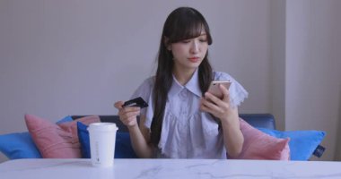 Oturma odasında elinde Card ve Smartphone olan bir Japon kadın. Yüksek kalite 4K görüntü. Tokyo Japonya 06.19.2025
