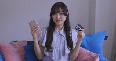 Oturma odasında elinde Card ve Smartphone olan bir Japon kadın. Yüksek kalite 4K görüntü. Tokyo Japonya 06.19.2025